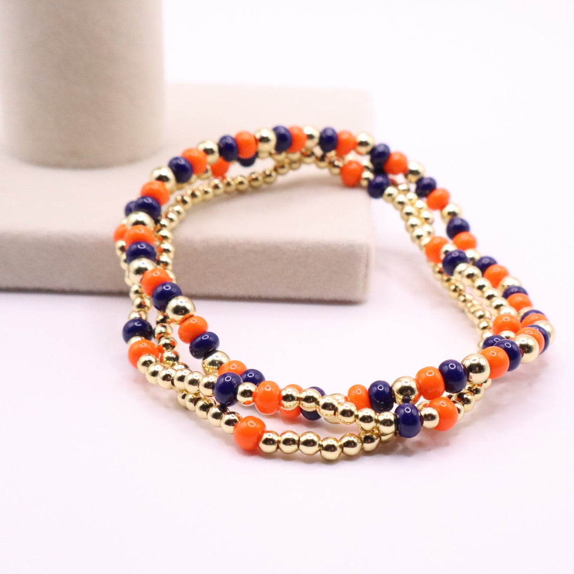 Three orange, navy blue and gold beaded bracelets on a light background