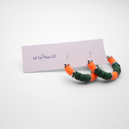 Orange and green heishi bead hoop earrings with silver accents hanging on a minimalist jewelry stand against a white background