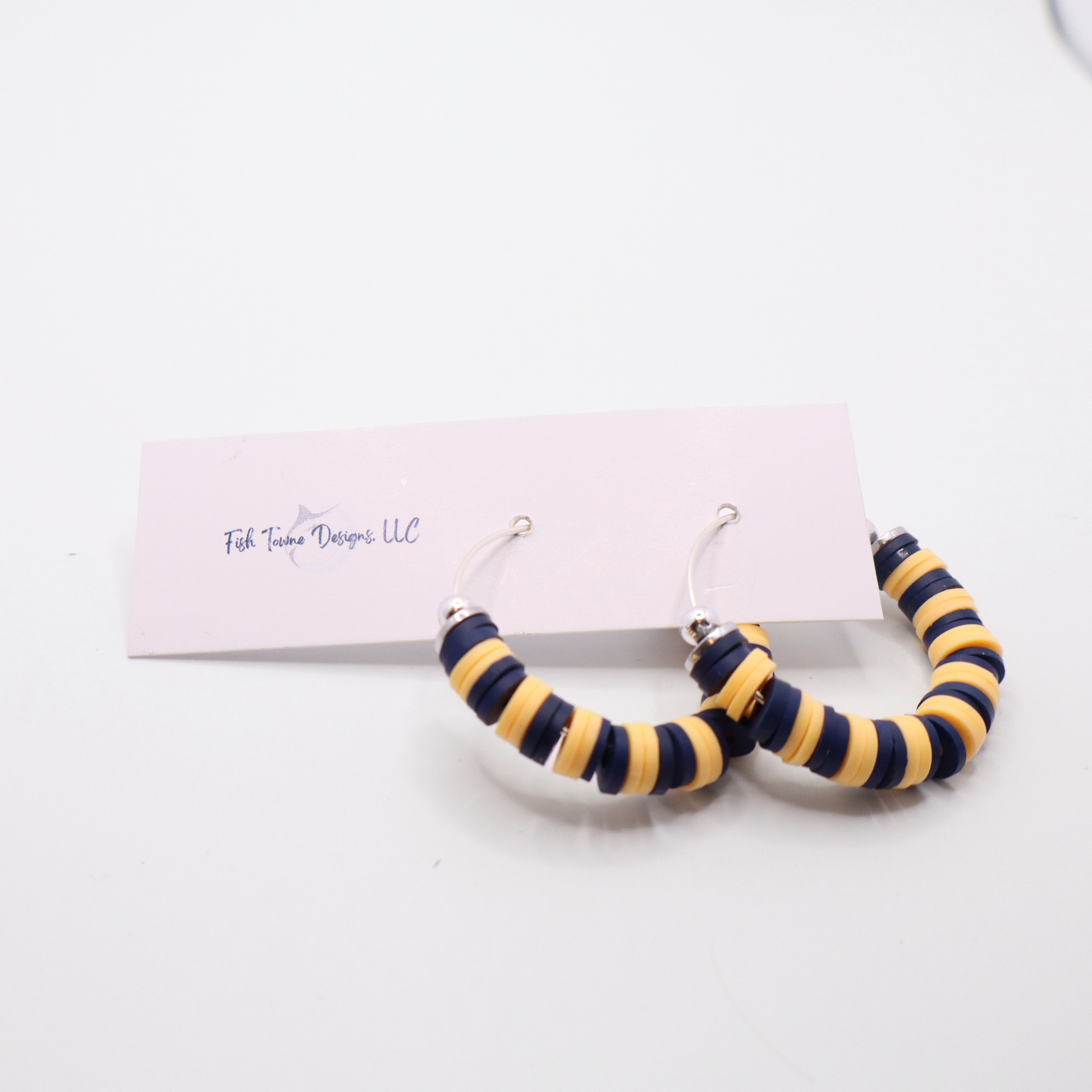 Navy and gold heishi bead hoop earrings with gold accents displayed on a branded card against a white background