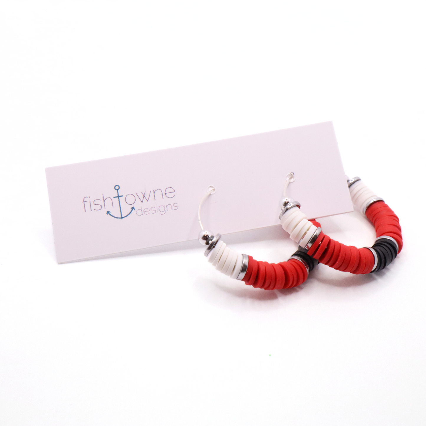 Red, white, and black heishi bead hoop earrings with silver accents hanging on a minimalist jewelry stand against a white background