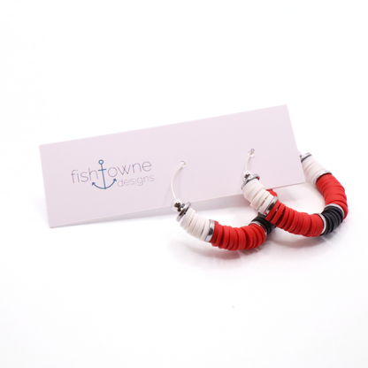 Red, white, and black heishi bead hoop earrings with silver accents hanging on a minimalist jewelry stand against a white background