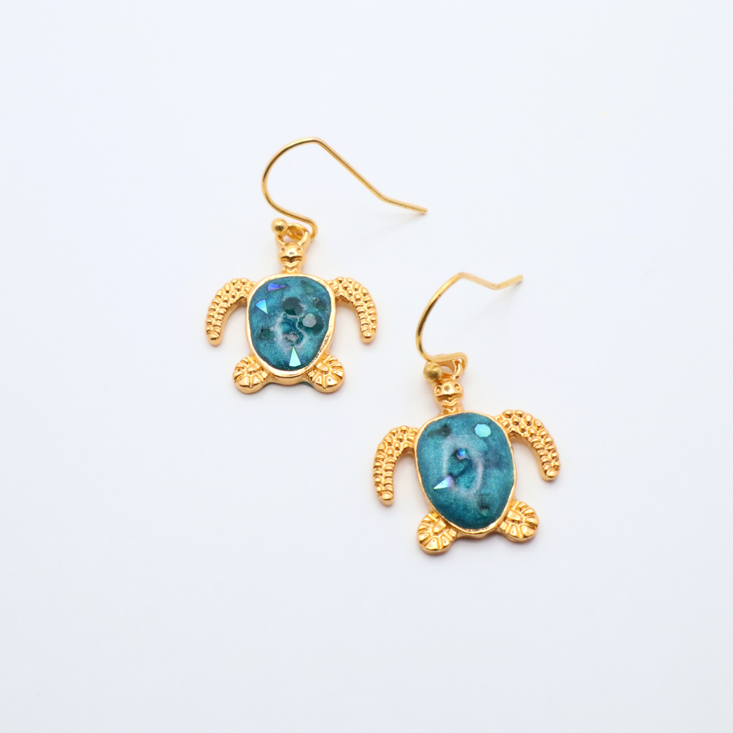 Turtle-shaped earrings with teal blue resin and gold frames on a white gray background