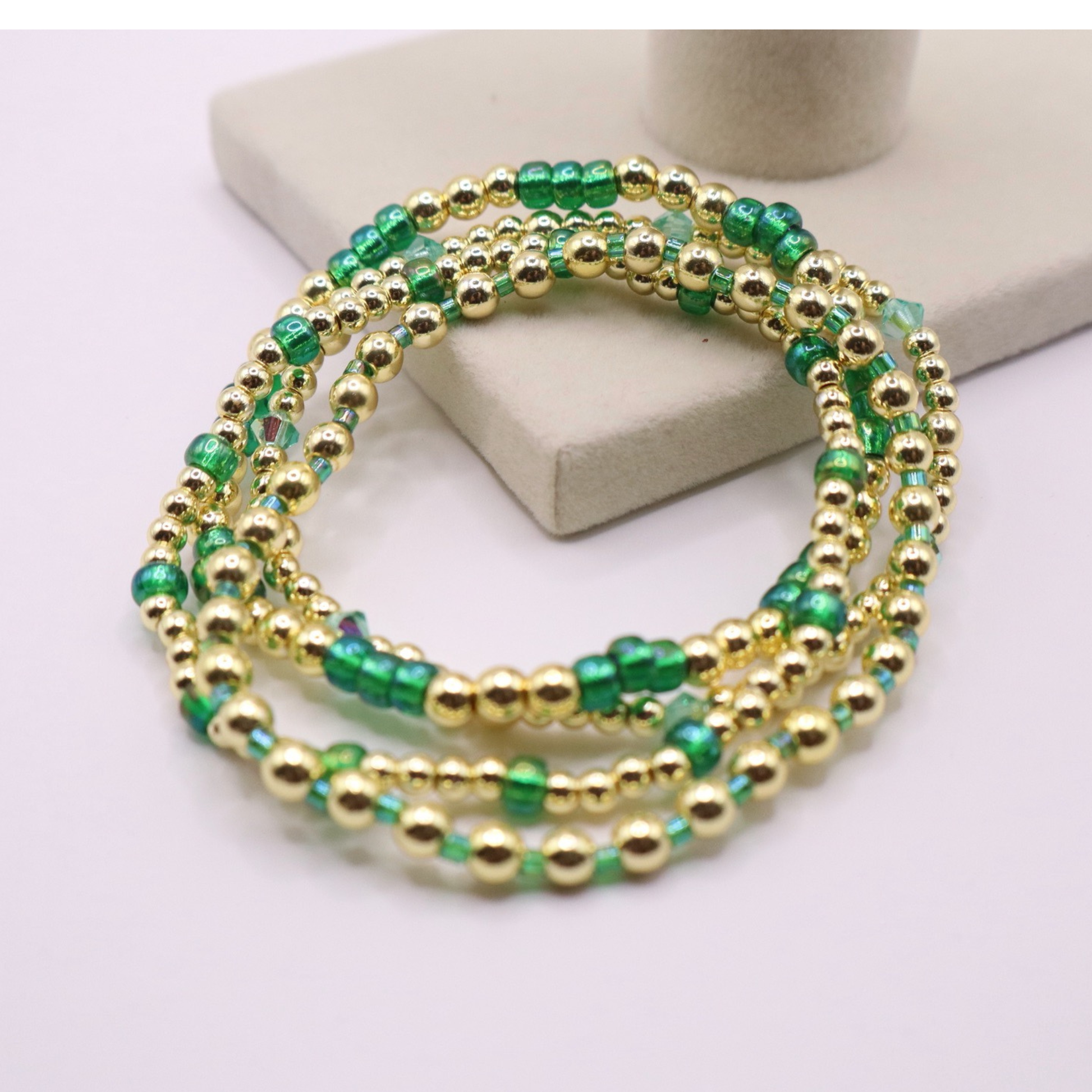 Handmade bracelet stack with green Preciosa seed beads, iridescent crystal accents, and polished gold-tone hematite beads on a clean white background.