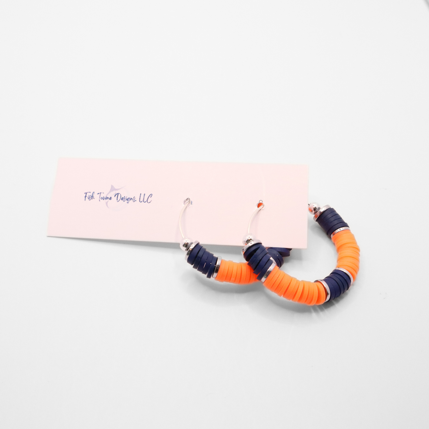 Navy blue and white heishi bead hoop earrings with silver accents hanging on a minimalist jewelry stand against a white background