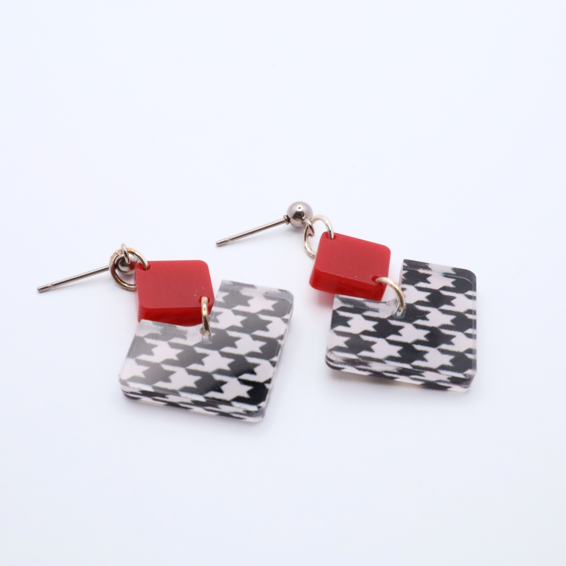 Pair of earrings with red square and houndstooth patterned rectangular drops on a white background