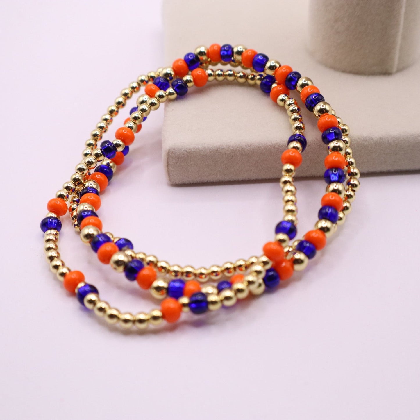 Three beaded bracelets with gold, blue, and orange beads on a white background