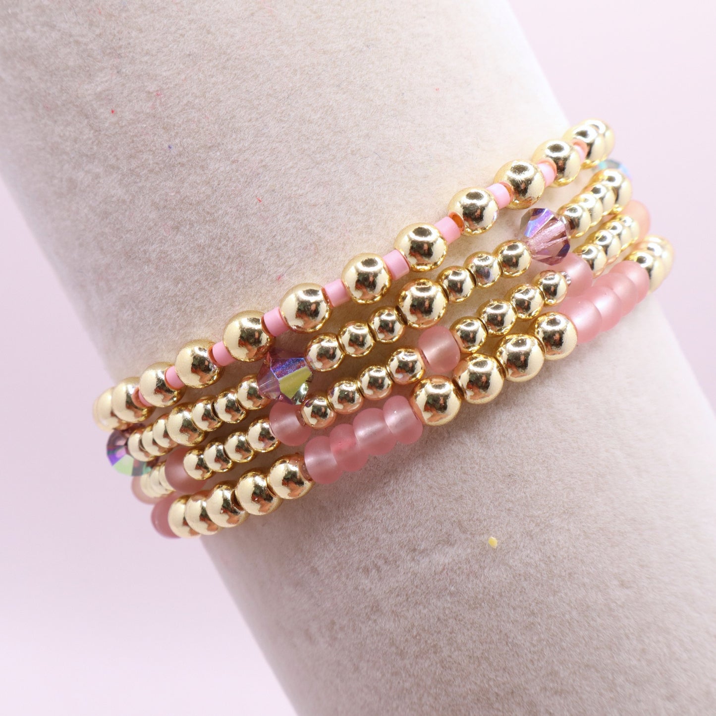 Layered blush pink bracelet stack displayed on a jewelry stand.