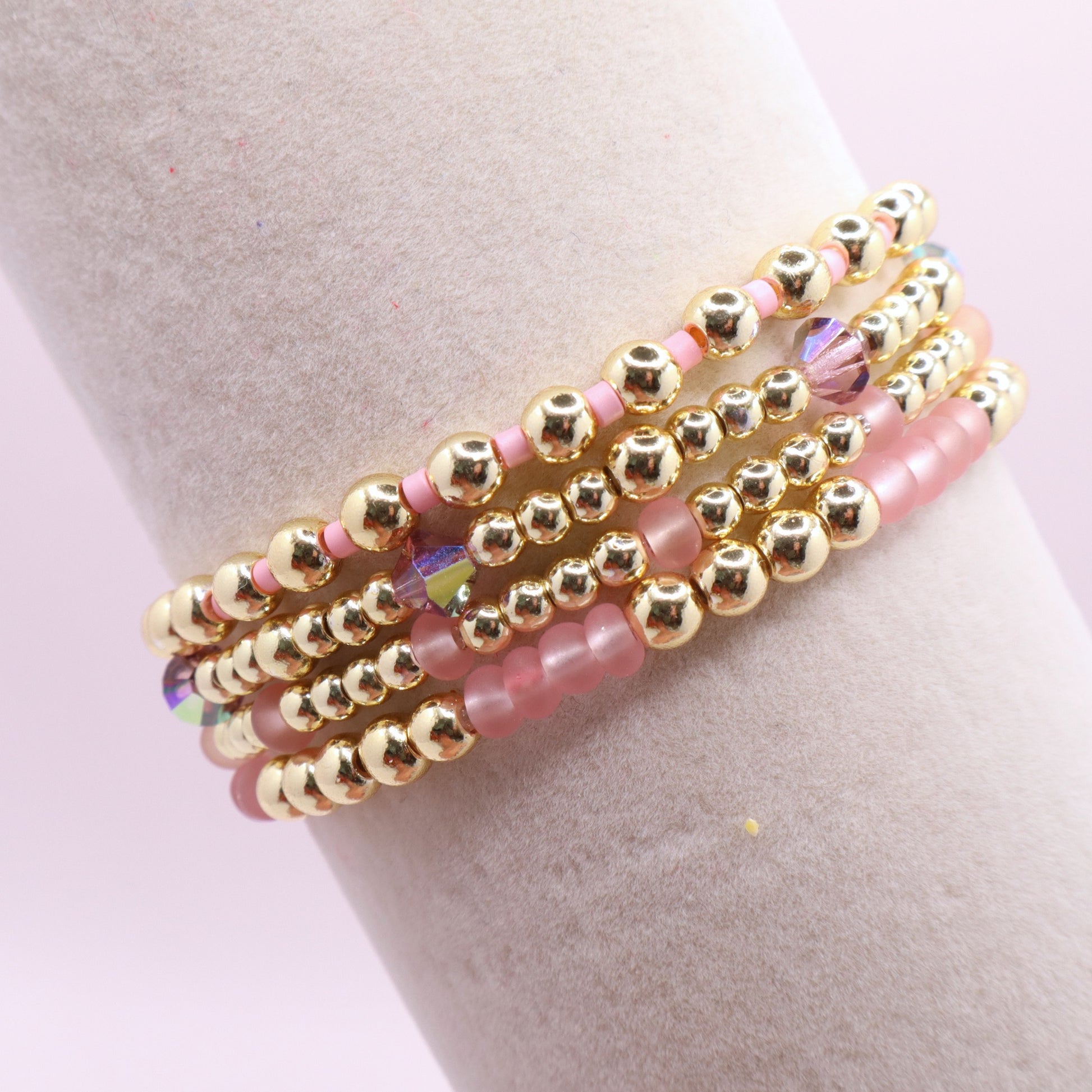 Layered blush pink bracelet stack displayed on a jewelry stand.