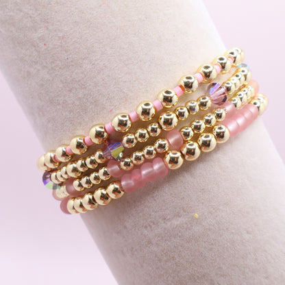 Layered blush pink bracelet stack displayed on a jewelry stand.