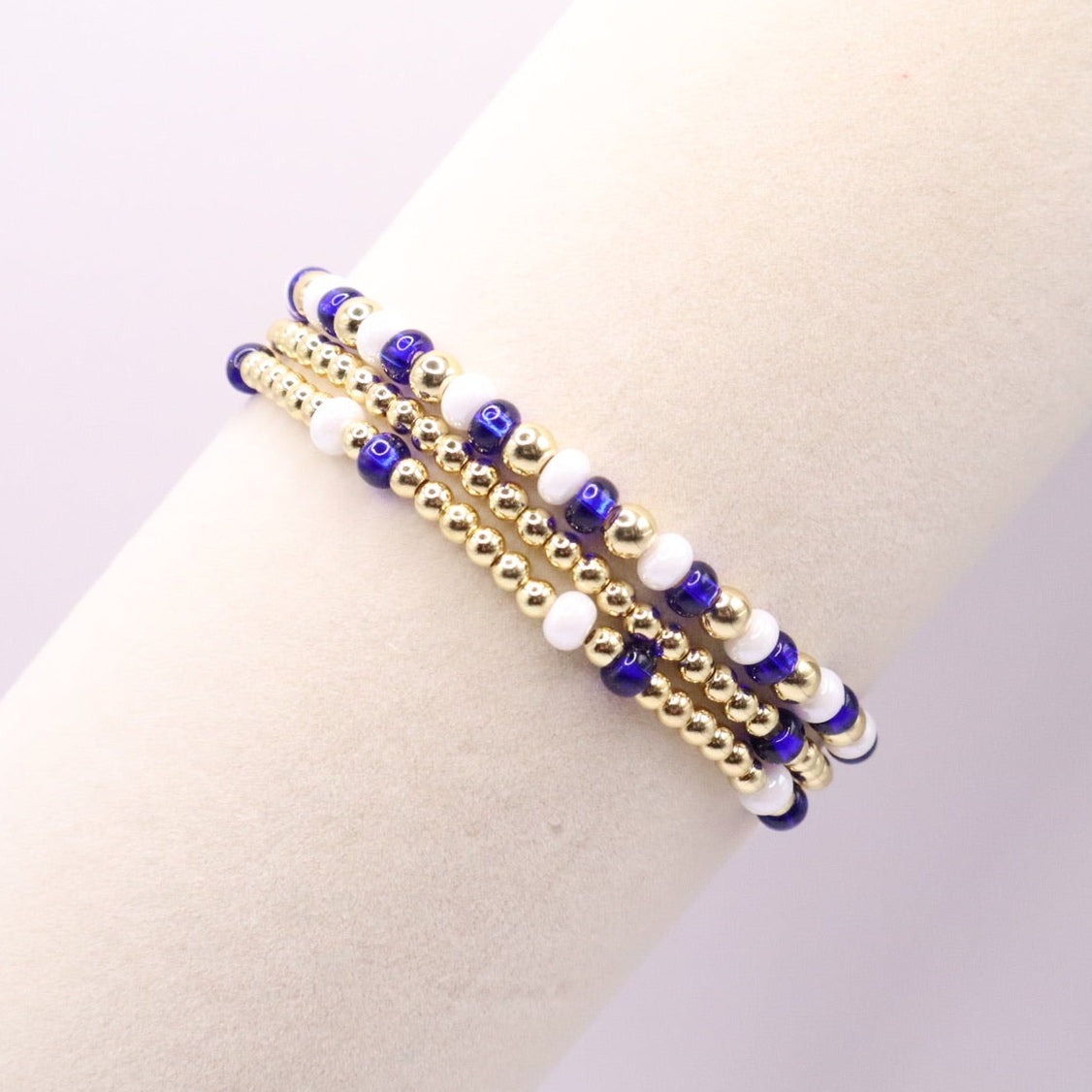 Gold bracelet with blue and white beads on a wrist against a neutral background