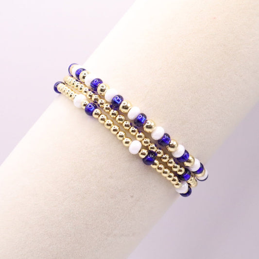 Gold bracelet with blue and white beads on a wrist against a neutral background