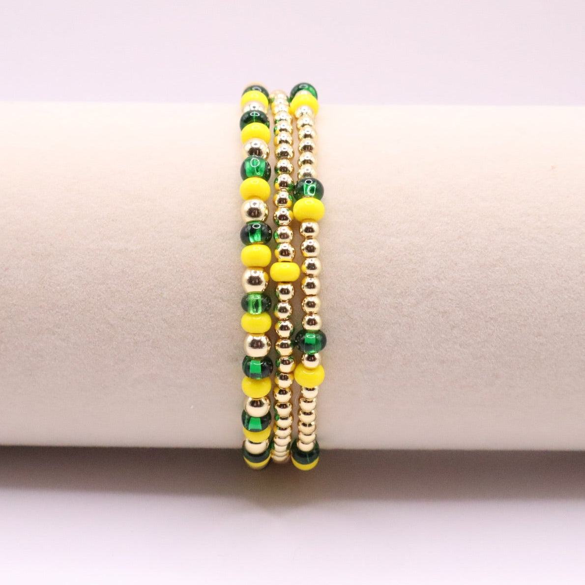 Set of three green, yellow, and gold beaded bracelets on a white surface