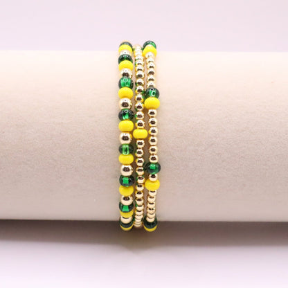Set of three green, yellow, and gold beaded bracelets on a white surface
