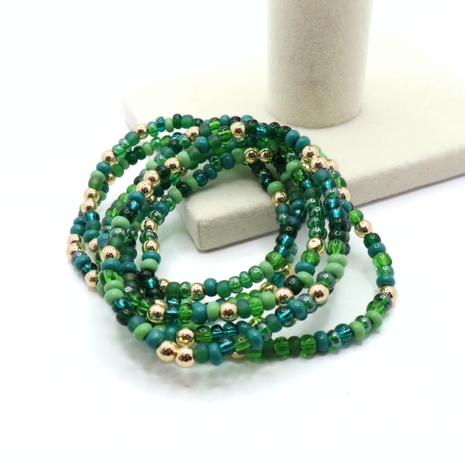 Set of six green beaded bracelets with gold accents on a white surface