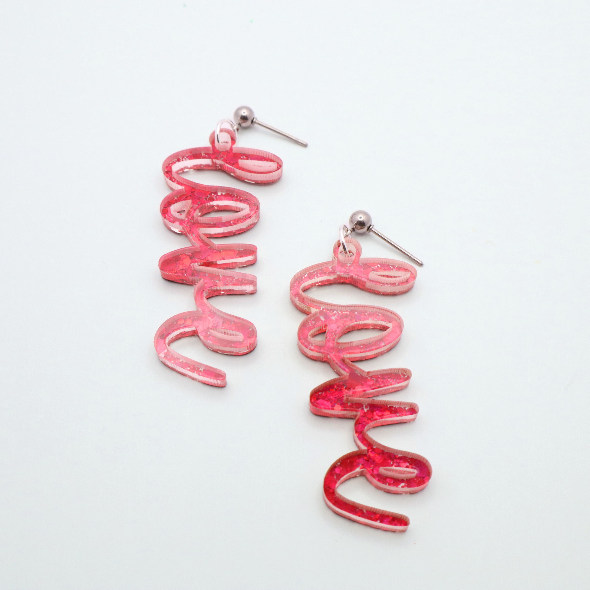 Pink glitter 'love' earrings on a white gray background