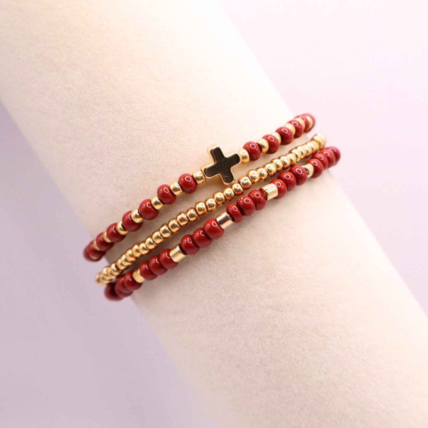 Three rust and gold beaded bracelets on a mannequin wrist with a light purple background