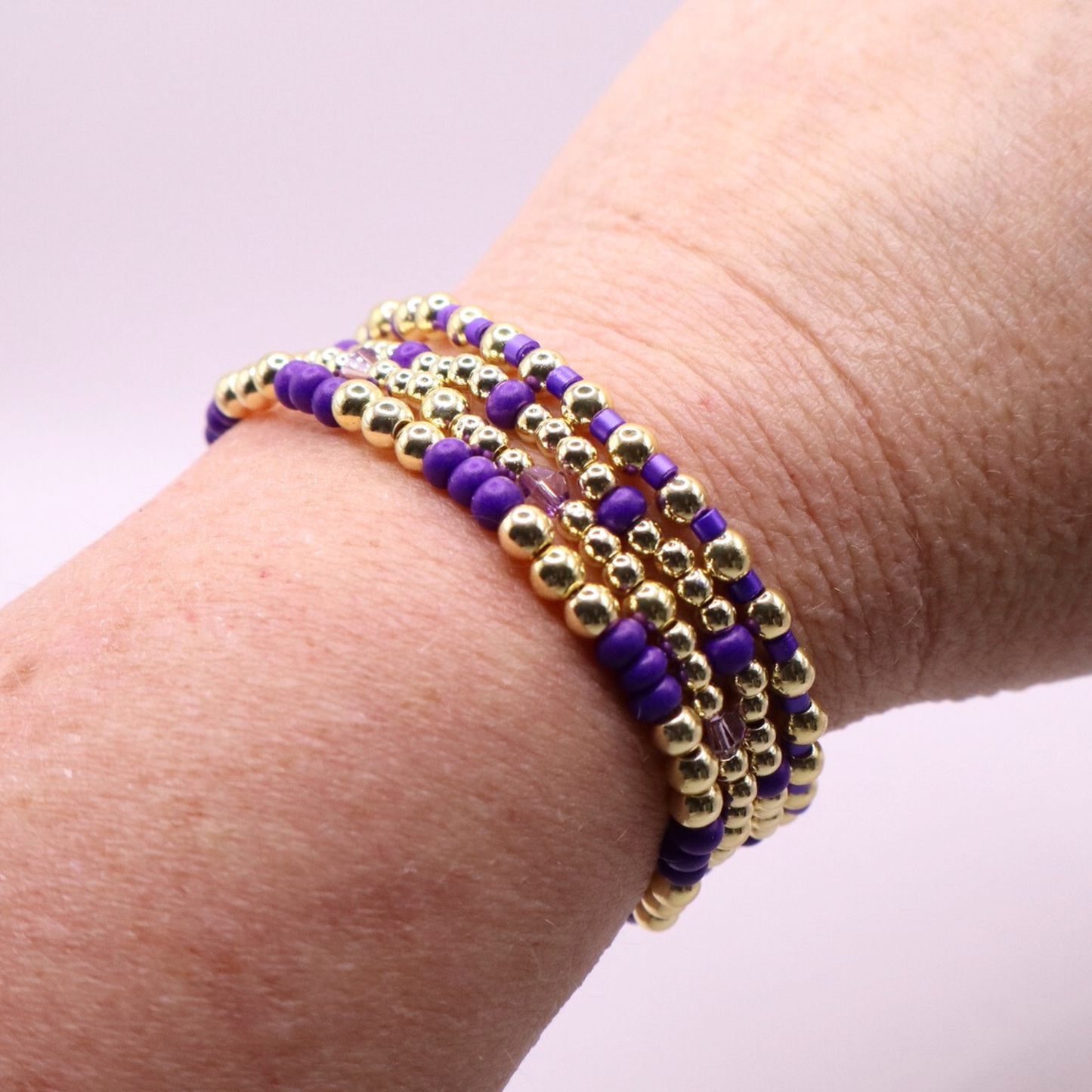 Elegant stack of stretch bracelets featuring rich purple Preciosa seed beads, faceted crystal details, and gold-tone hematite accent beads on a clean white background.