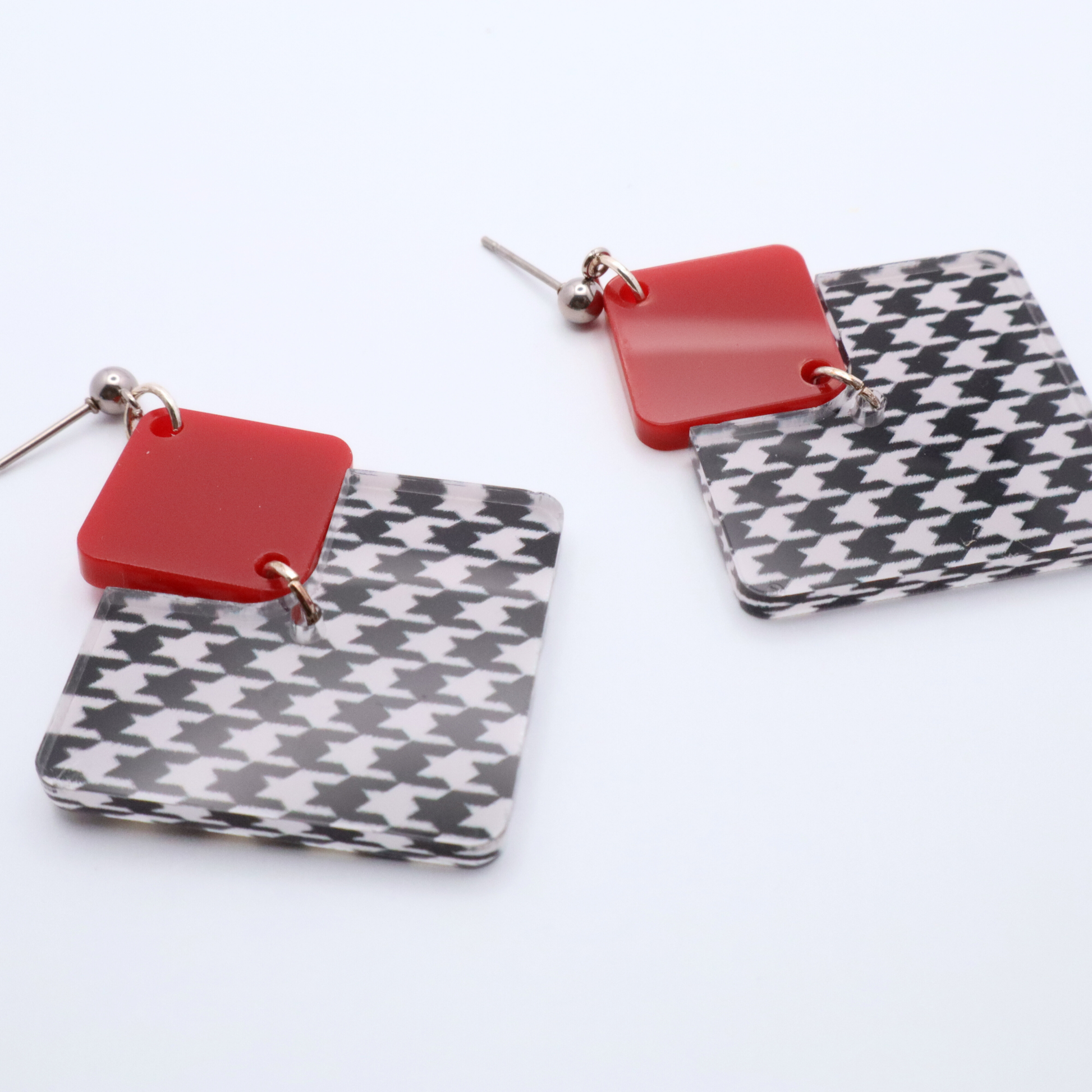 Pair of earrings with red square and houndstooth pattern on a white background