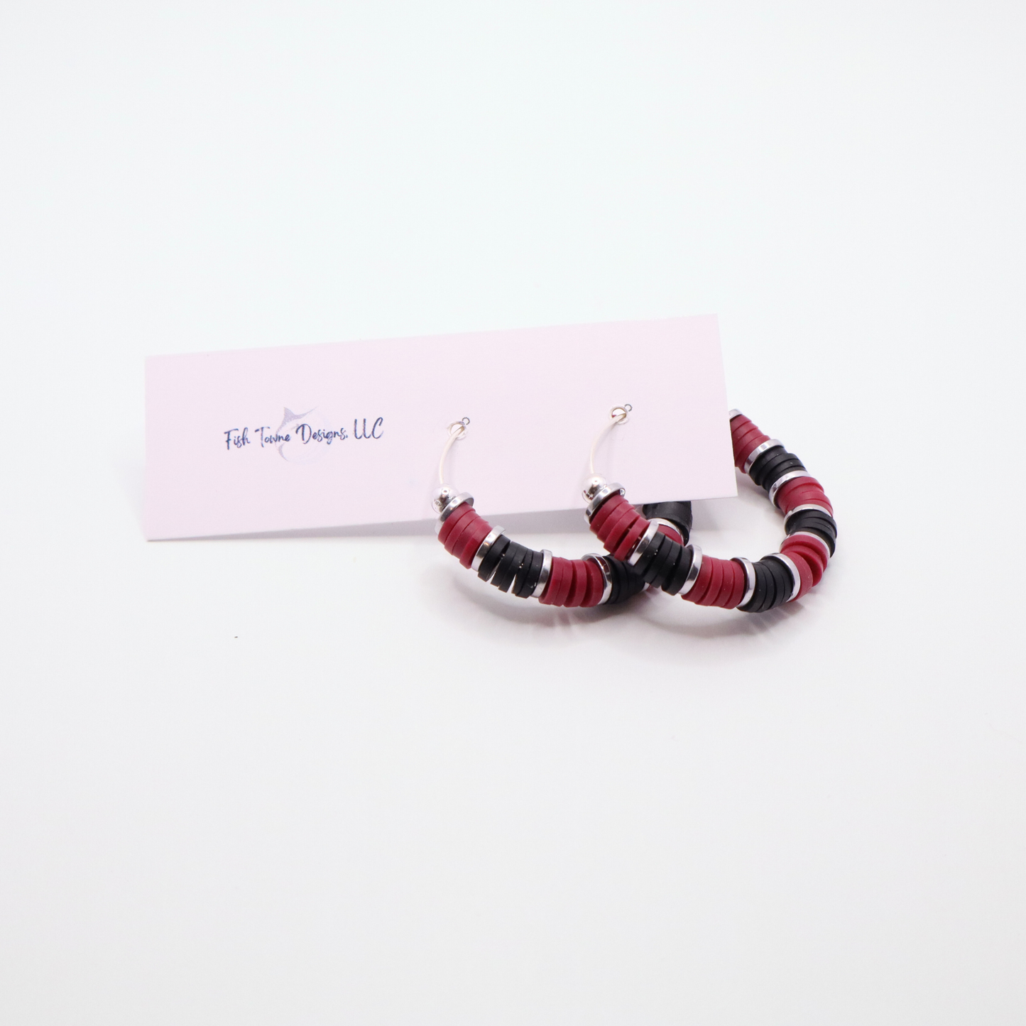 Handmade maroon and black polymer clay heishi bead hoop earrings with silver spacers shown on a white background with display card