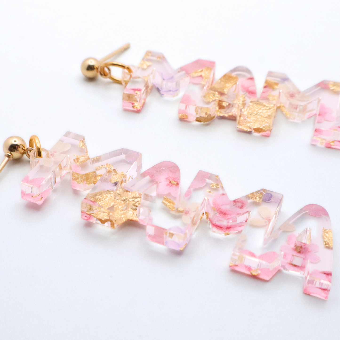 Pair of mama earrings with pink and gold accents on a white background