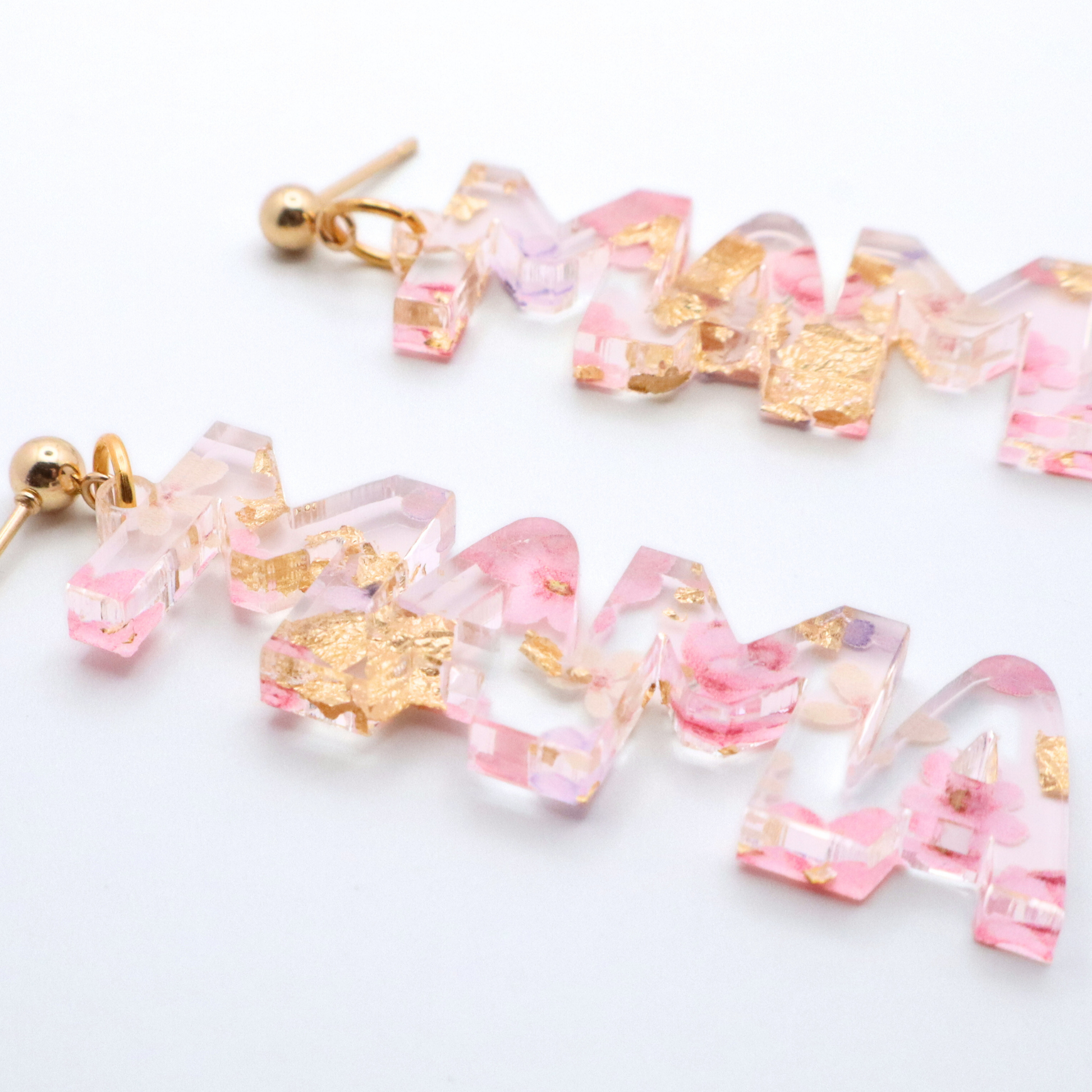 Pair of mama earrings with pink and gold accents on a white background