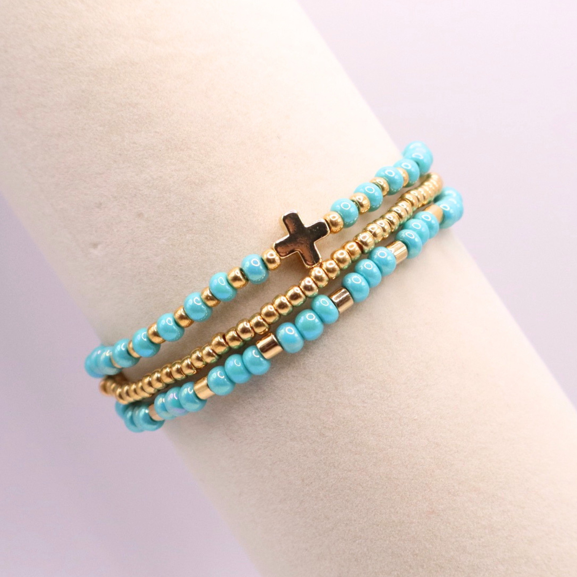Turquoise beaded bracelet stack with gold accents and a gold cross charm on a mannequin wrist against a light background