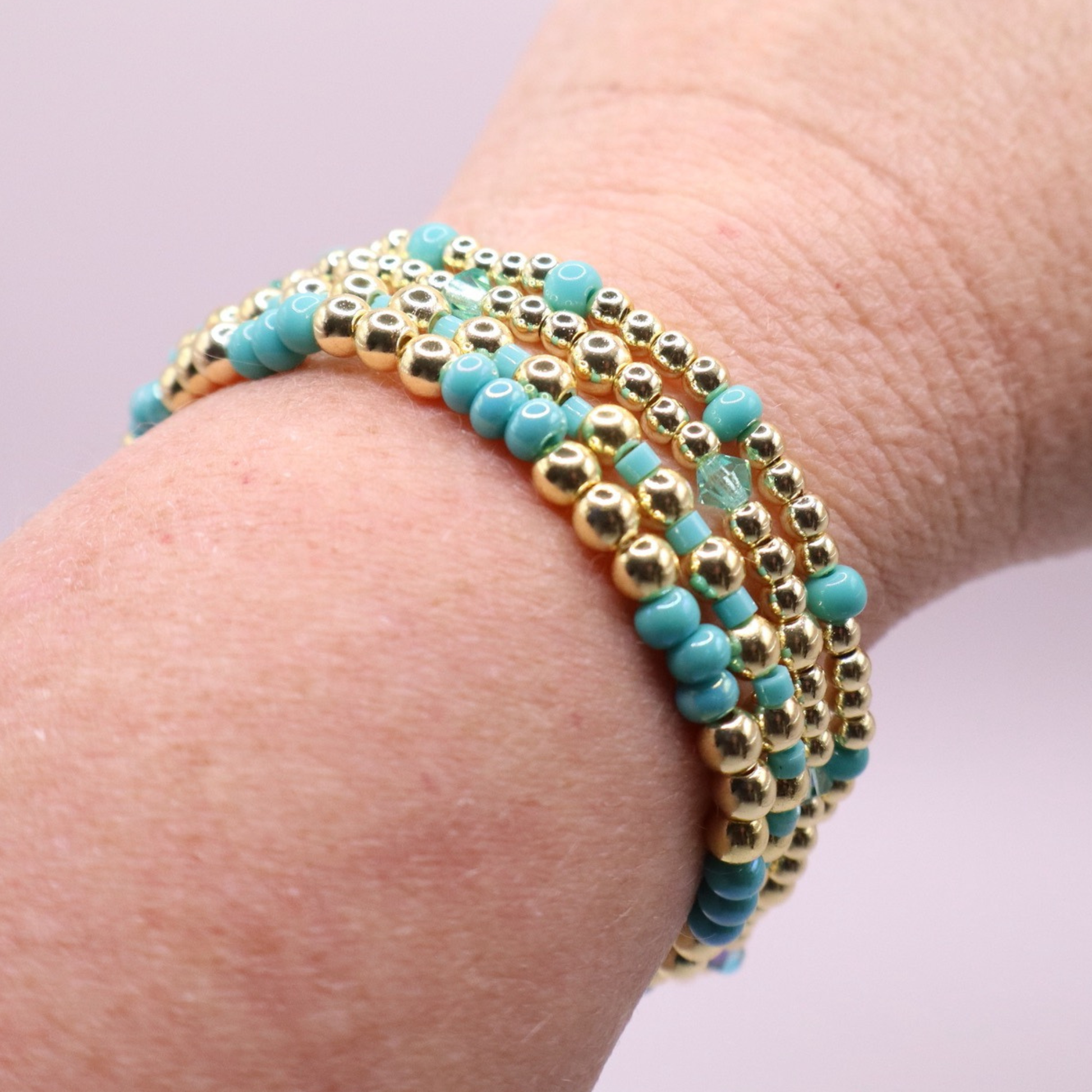 Layered bracelet stack with turquoise Preciosa seed beads, shimmering crystal accents, and gold-tone hematite beads on a clean white background.