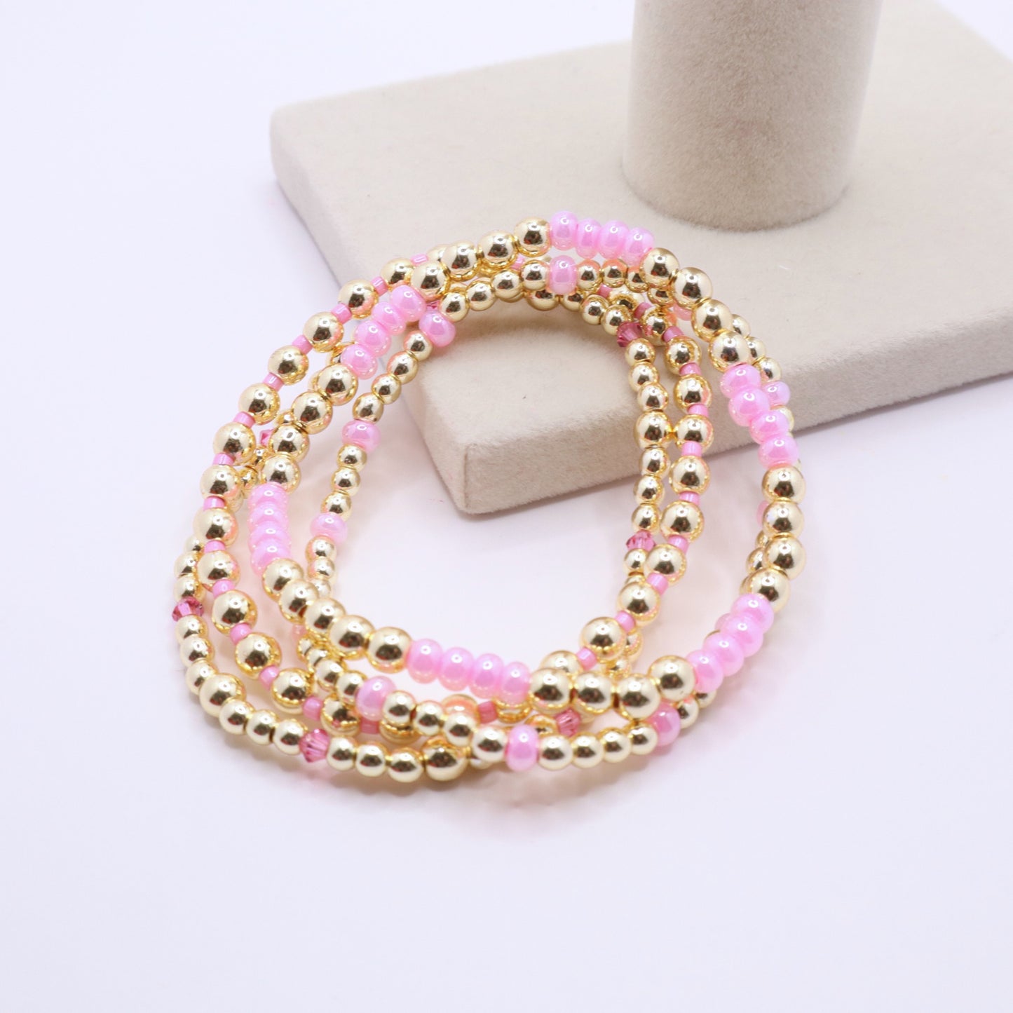 Three coordinating handmade bracelets featuring pink and gold bead combinations.