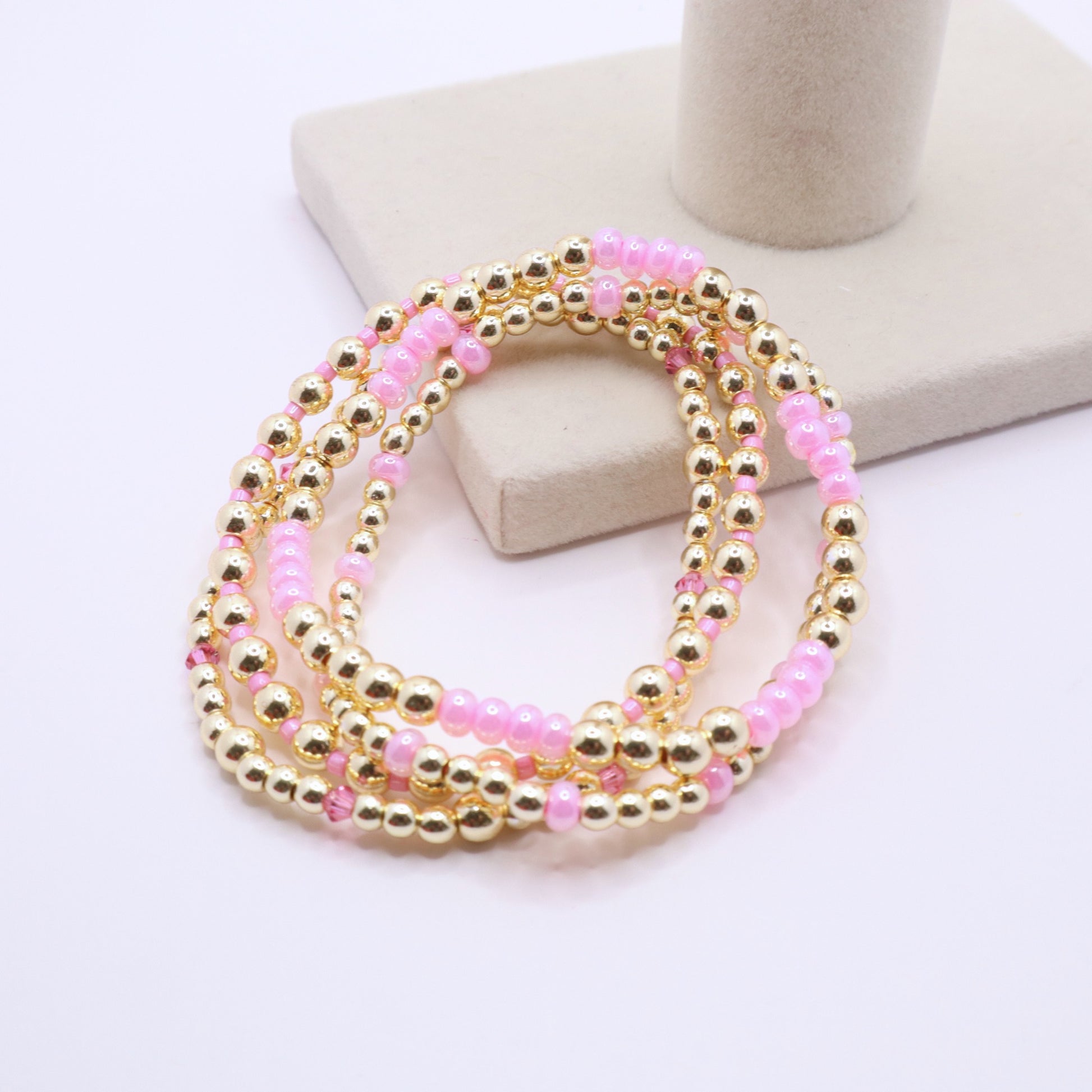 Three coordinating handmade bracelets featuring pink and gold bead combinations.