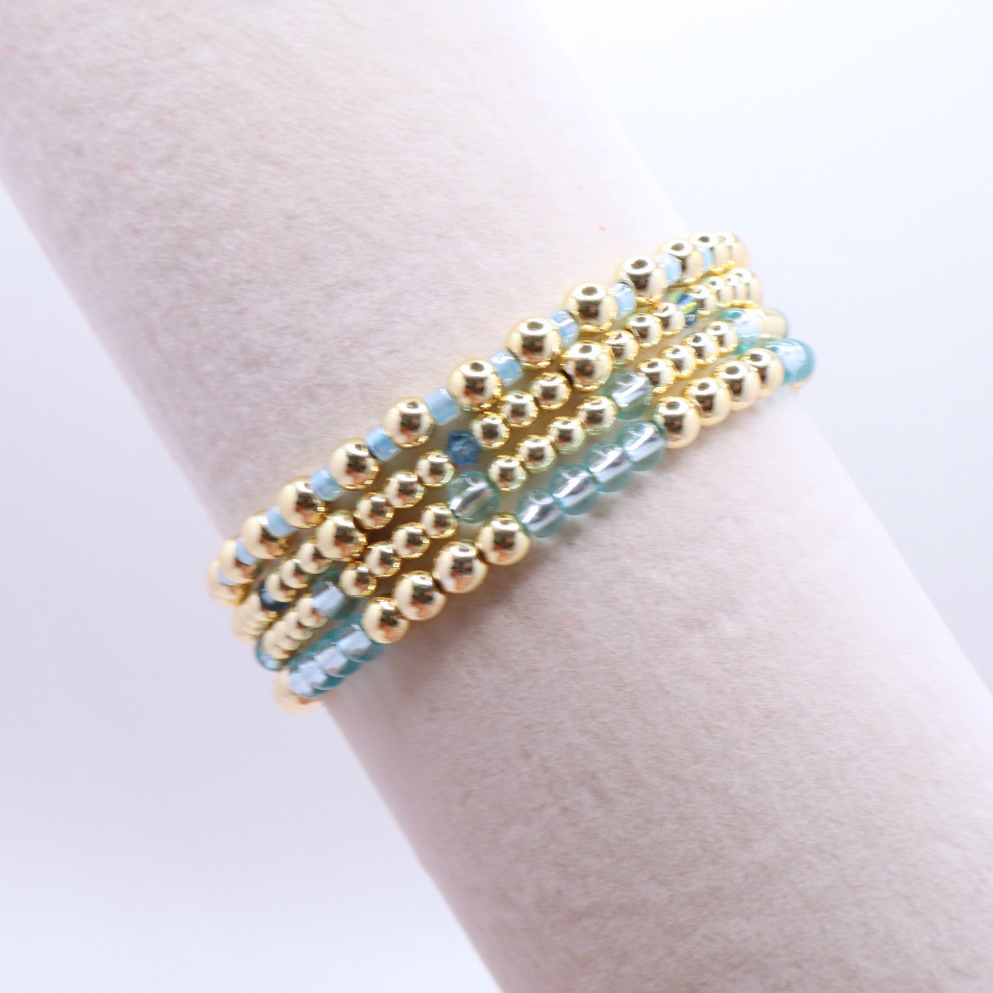 Layered blue and gold bracelet stack displayed on a jewelry stand.