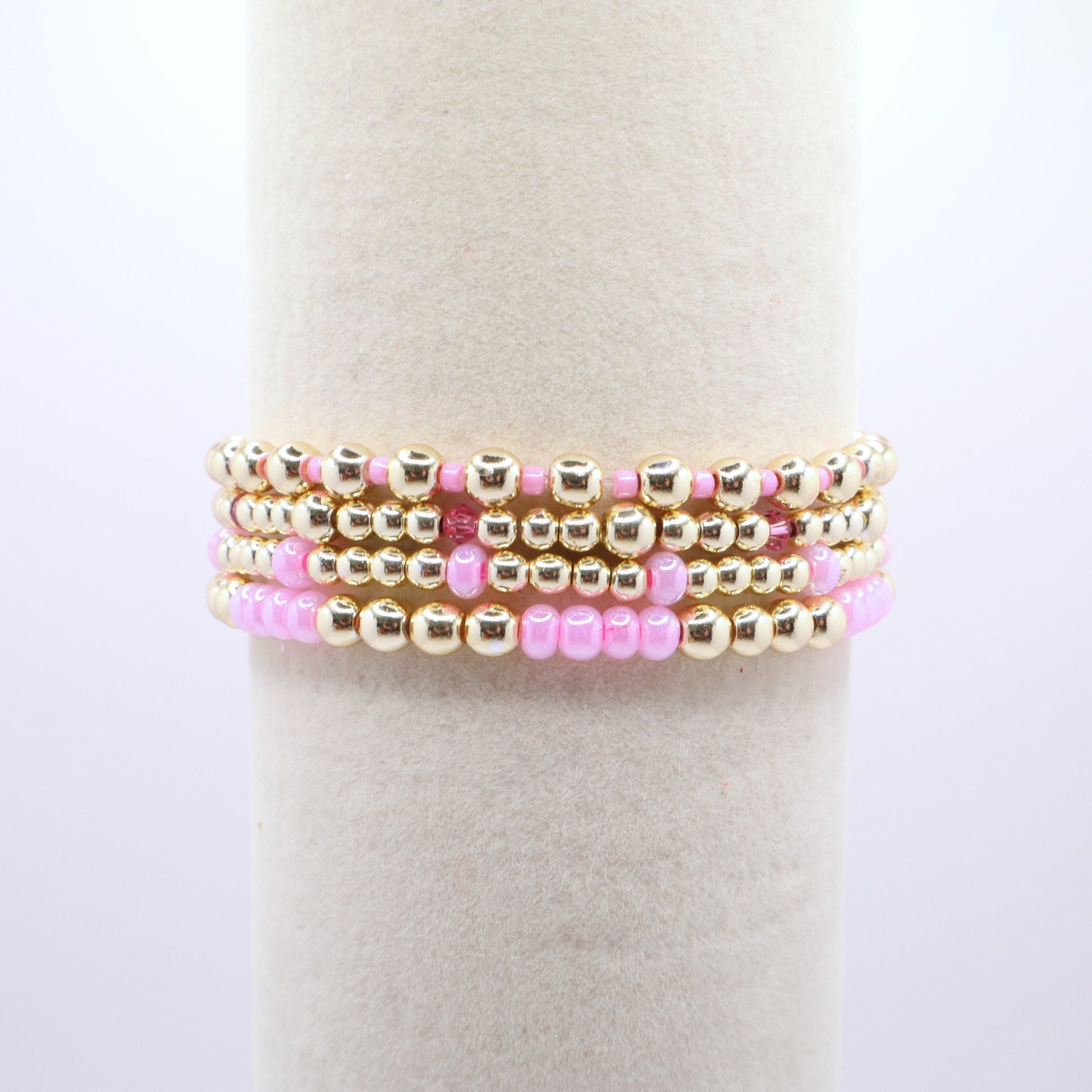 Layered pink and gold bracelet stack displayed on a jewelry stand.