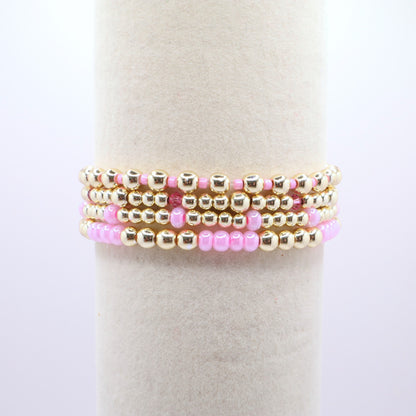 Layered pink and gold bracelet stack displayed on a jewelry stand.