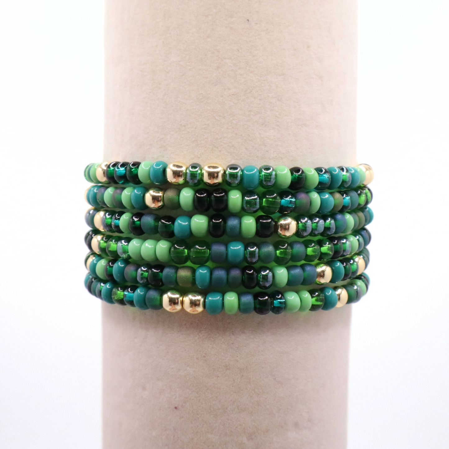 Stack of six green beaded bracelets on a white background