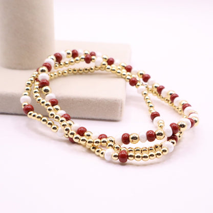 Three crimson, white and gold bracelets leaning on a beige box