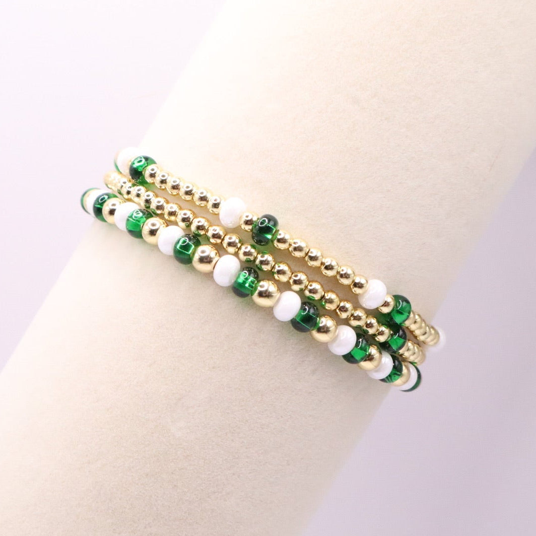 Gold bracelet with green and white beads on a mannequin arm against a light background