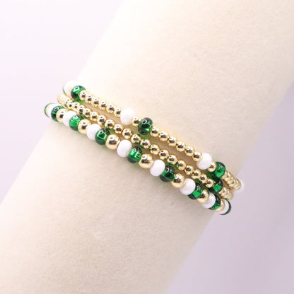 Gold bracelet with green and white beads on a mannequin arm against a light background