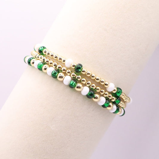 Gold bracelet with green and white beads on a mannequin arm against a light background