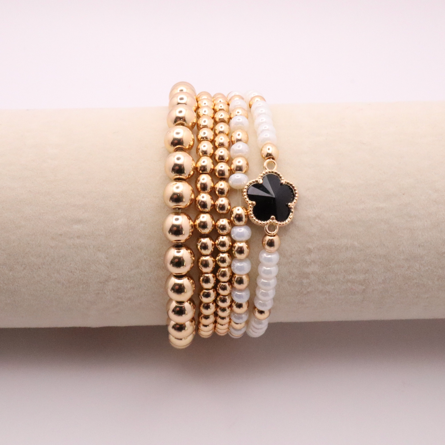 Set of 5 of gold toned beaded bracelets with white seed beads and hematite gold accents. One bracelet features a black clover charm. The bracelets are displayed on a white background.