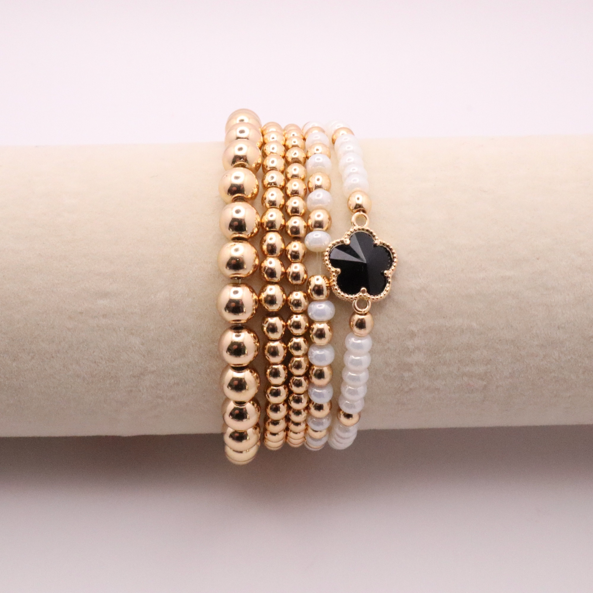 Set of 5 of gold toned beaded bracelets with white seed beads and hematite gold accents. One bracelet features a black clover charm. The bracelets are displayed on a white background.
