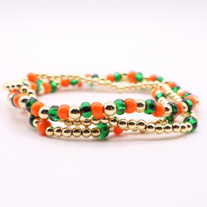 Stack of green, orange and gold beaded bracelets on a white background
