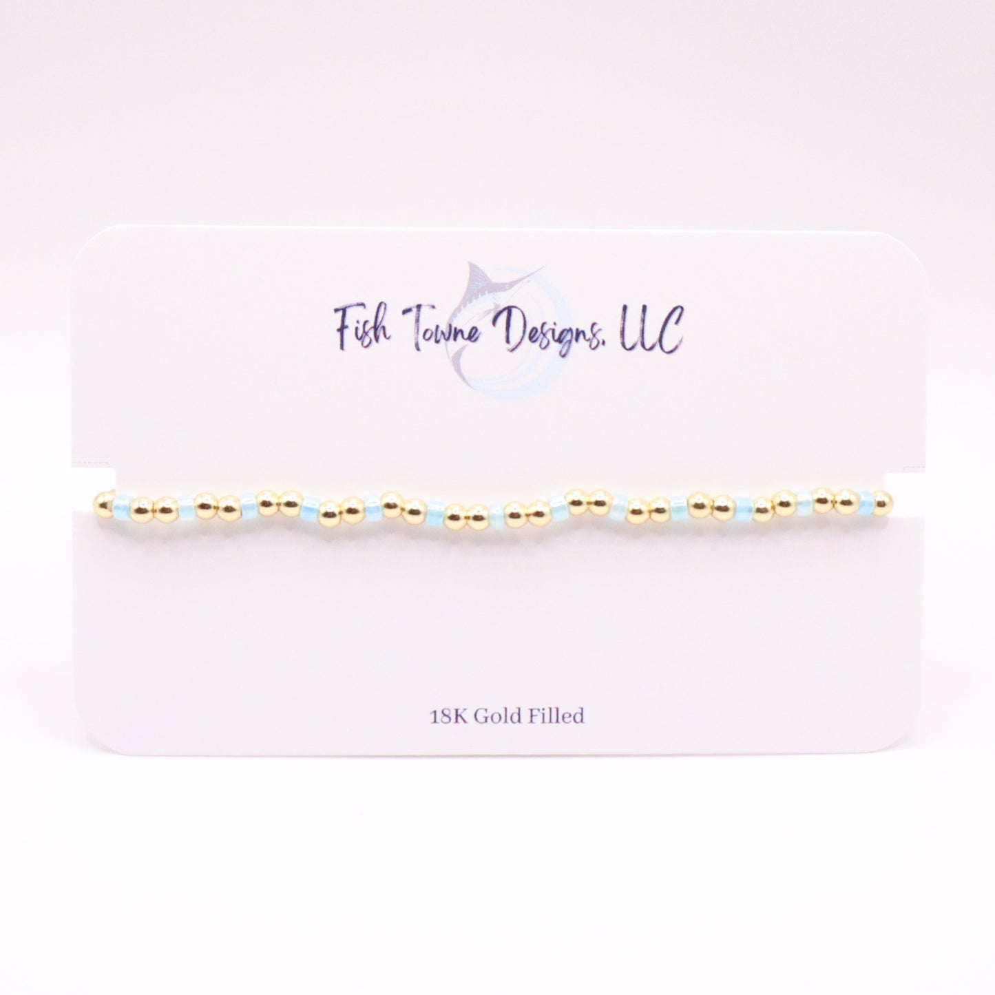 Gold and pale blue beaded bracelet on a white card with 'Fish Towne Designs, LLC' branding.