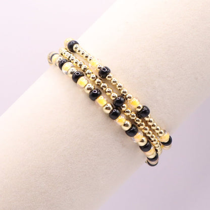 Three gold and black beaded bracelet on a bracelet display