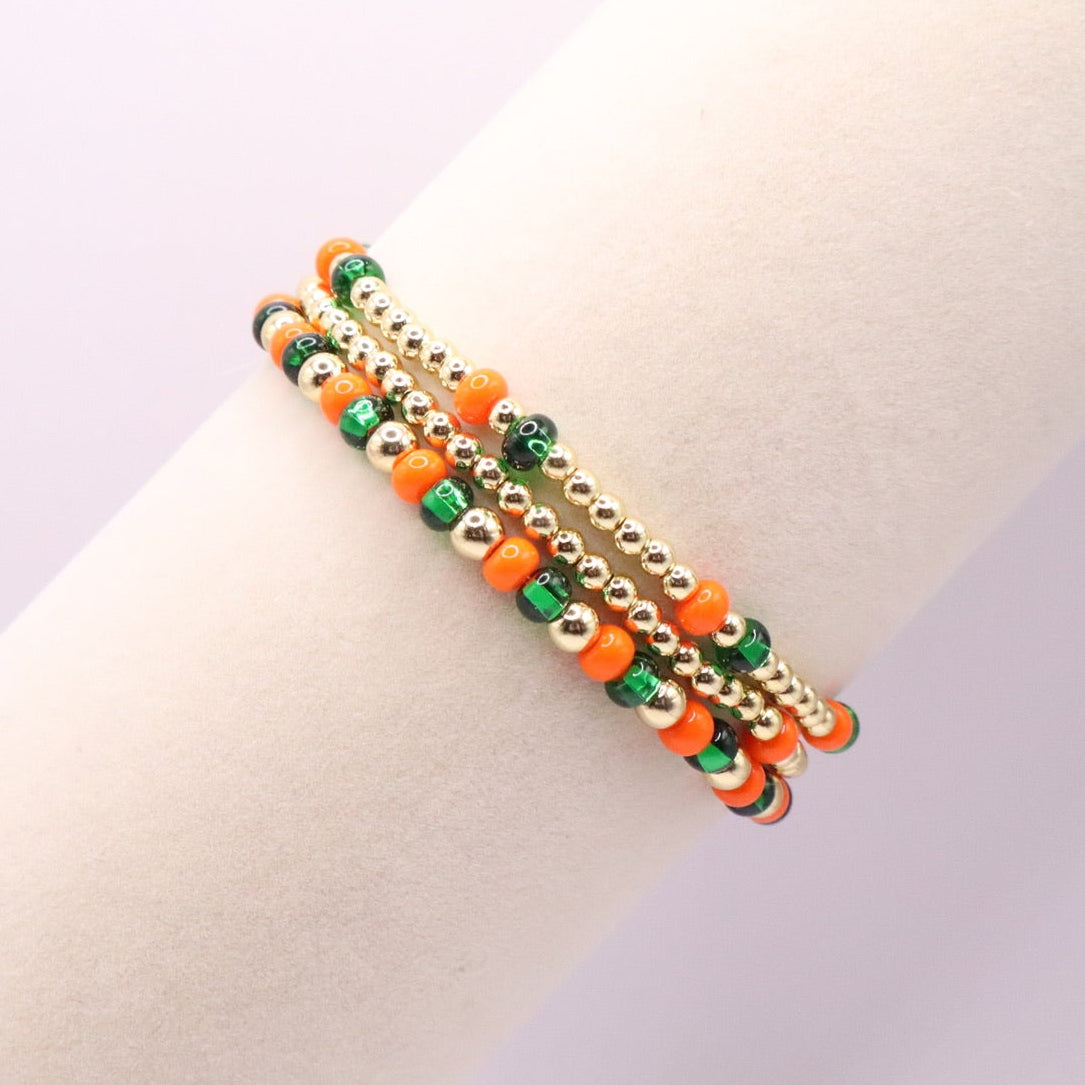 Three orange, green, and gold bracelets on a bracelet display