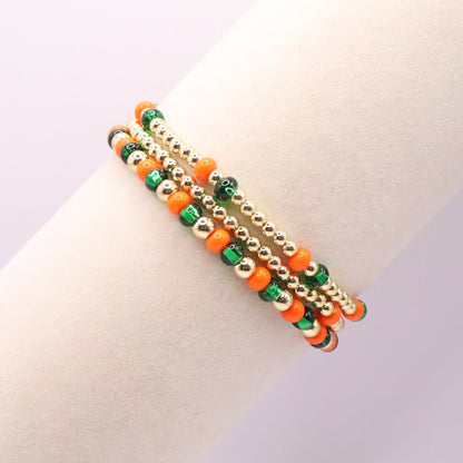Three orange, green, and gold bracelets on a bracelet display