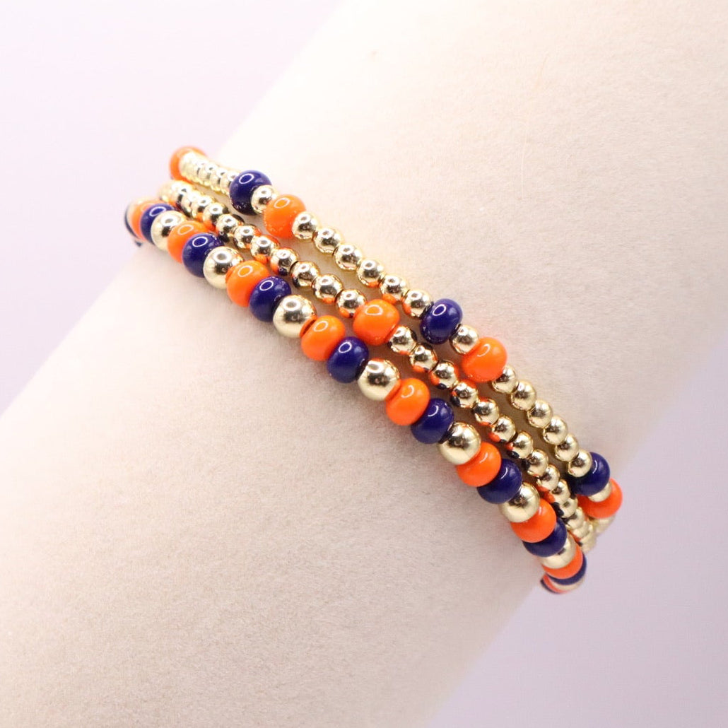 Three beaded bracelets in orange, blue, and gold on a wrist against a light background