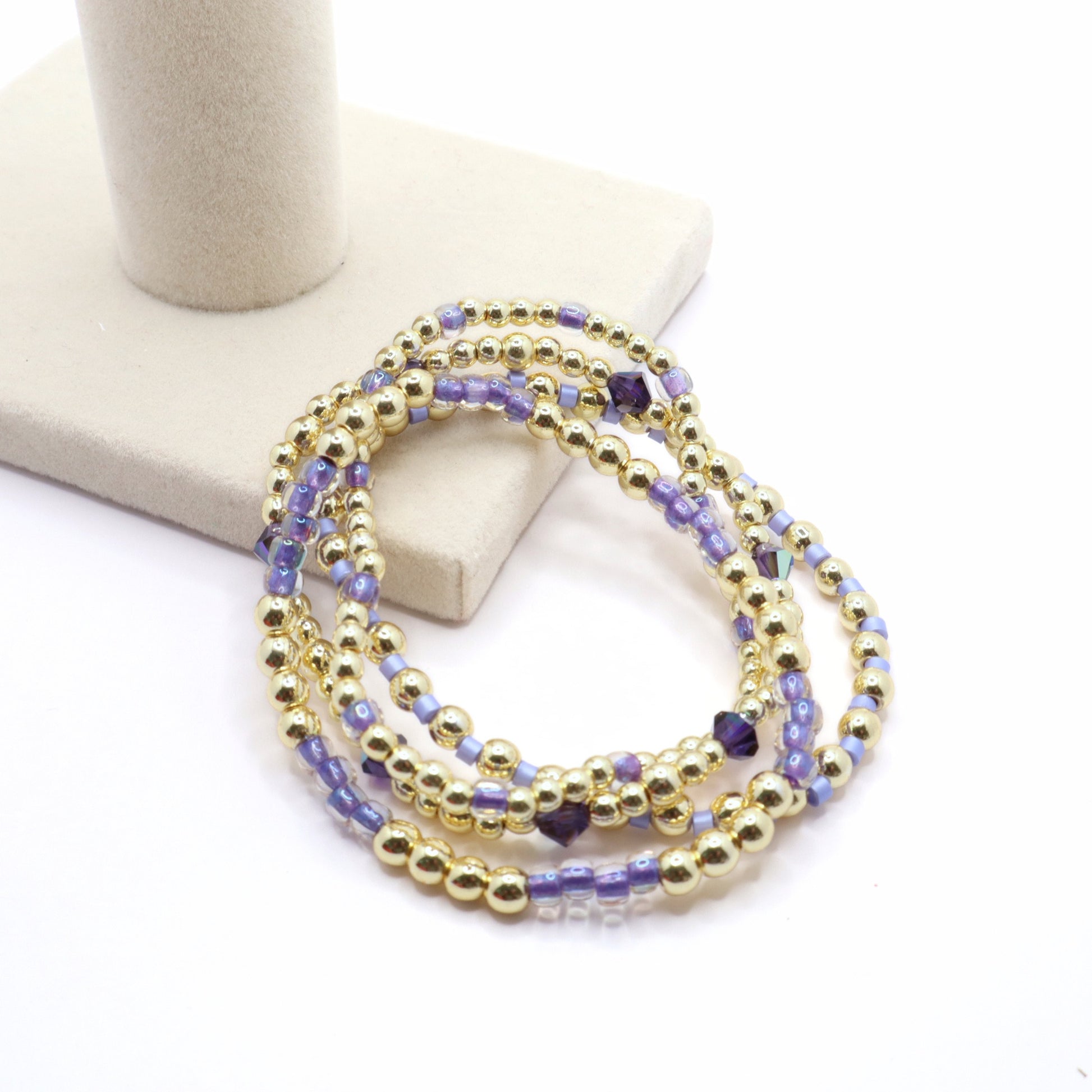 Layered gold and lavender stretch bracelets with shimmering crystal details.