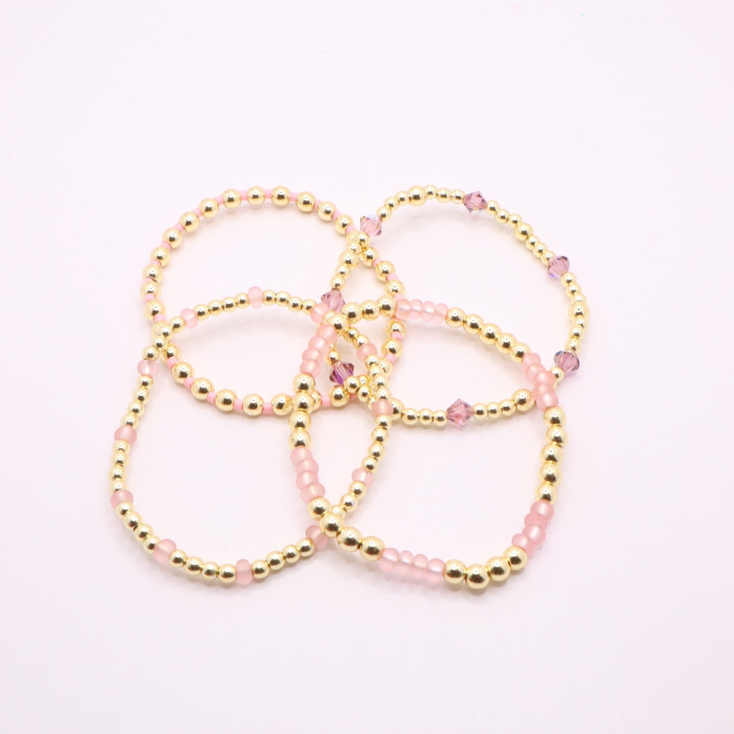 Feminine pink bracelet set featuring gold-tone beads and faceted crystals.