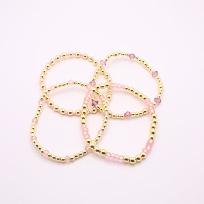 Feminine pink bracelet set featuring gold-tone beads and faceted crystals.