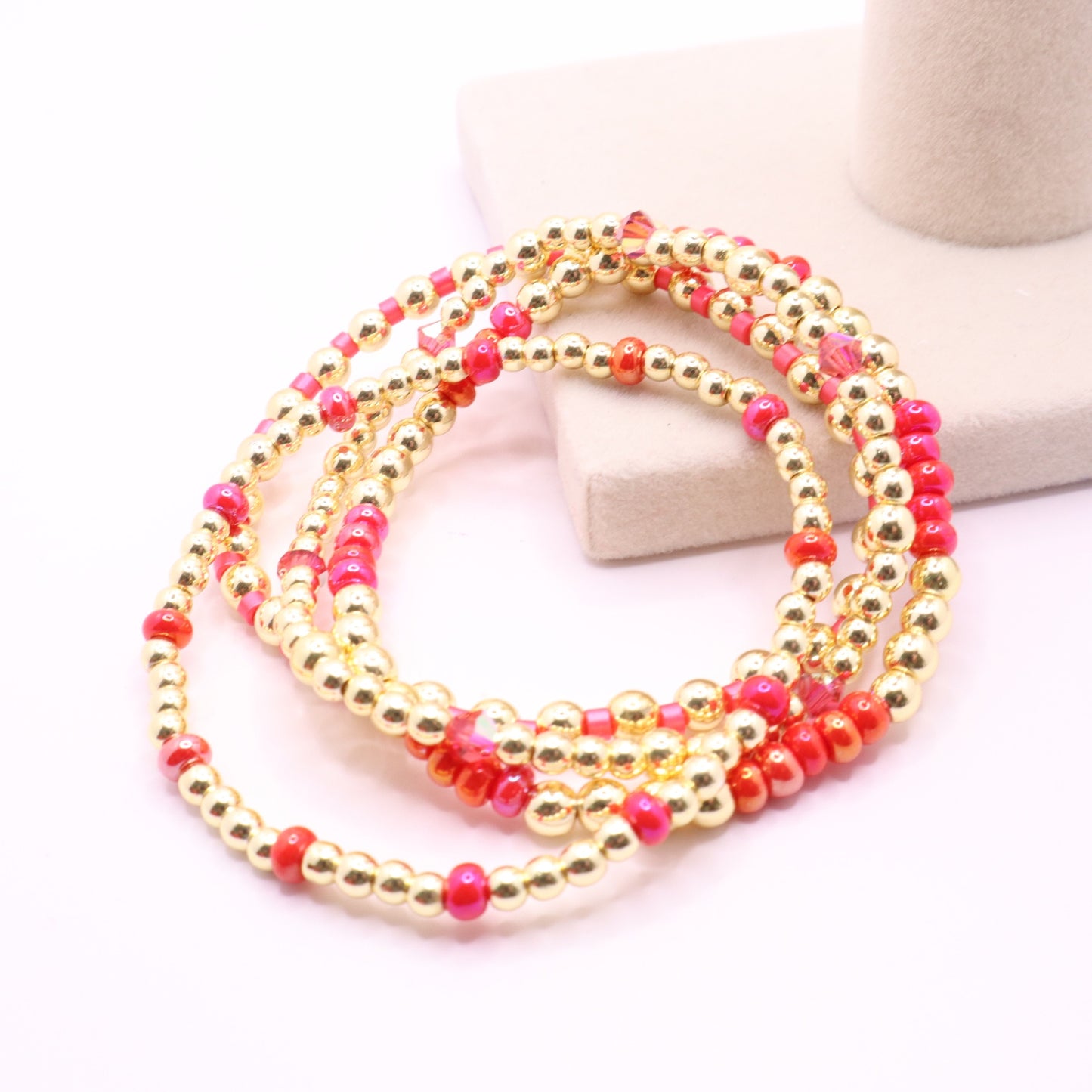 Colorful beaded bracelet stack featuring shades of coral, fuchsia, and gold.
