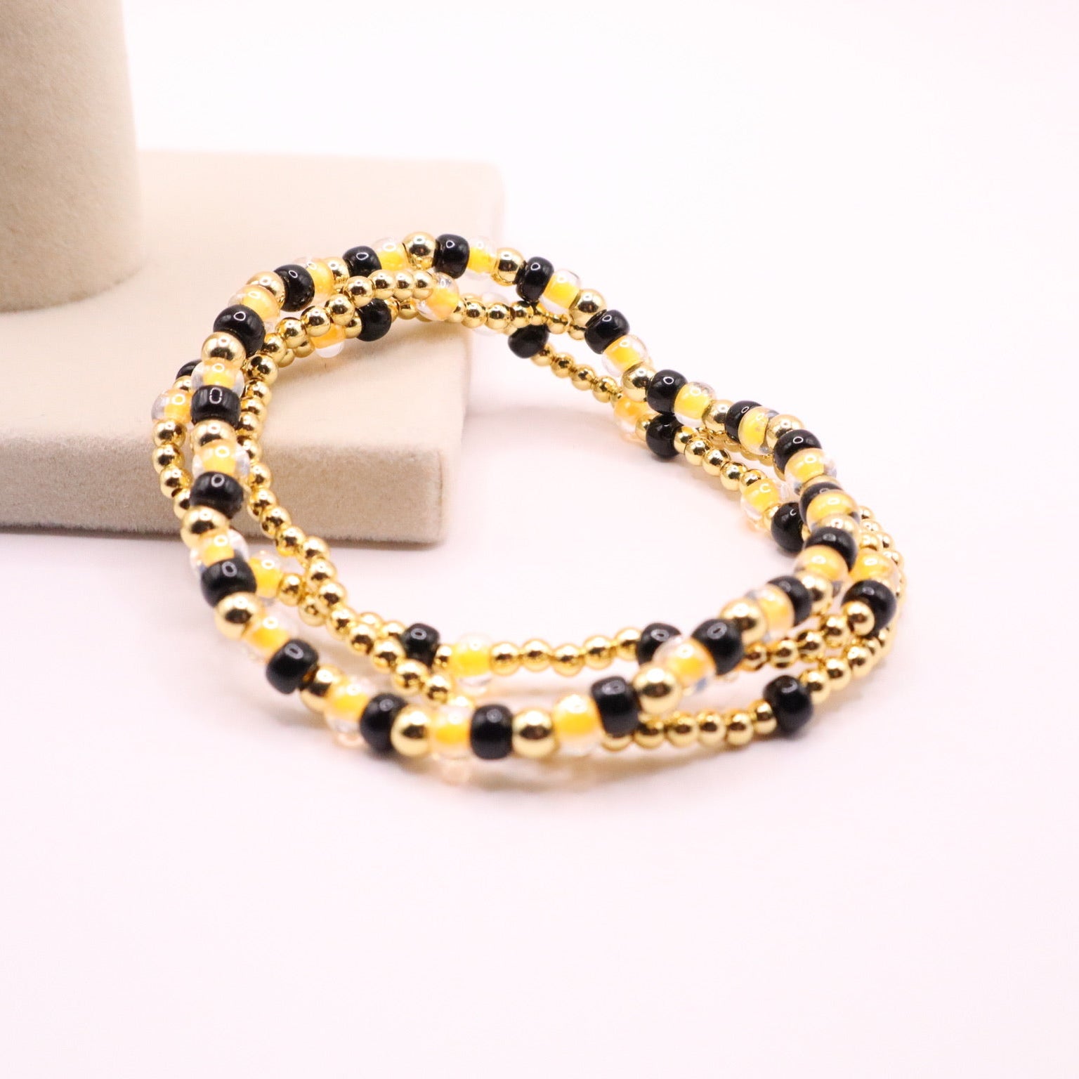Gold and black beaded bracelet on a white surface with a blurred background